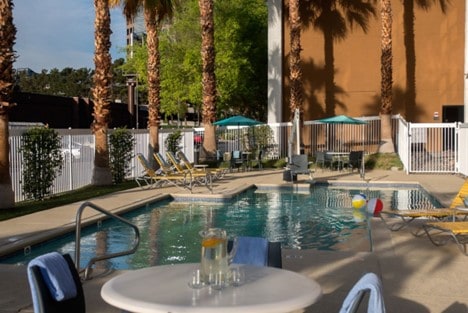 A table with a pitcher of water and glasses in front of the hotel pool.