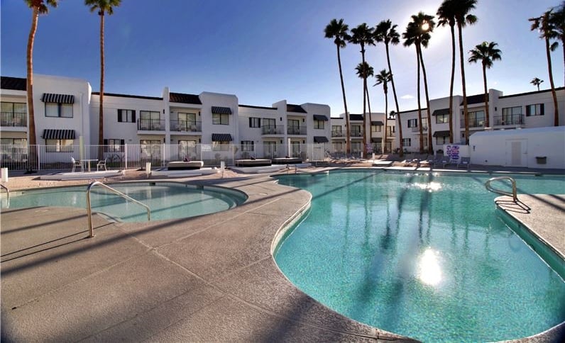 Hotel pool with hot tub on the left and tall palm trees on the right hand side.