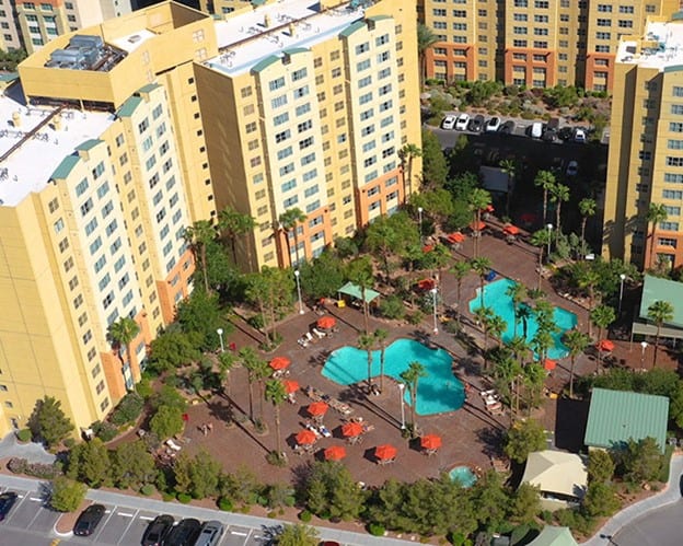 Aerial view of the two hotel pools with hotel towers on the left hand side and brightly colores sun umbrellas surrounding the pools.