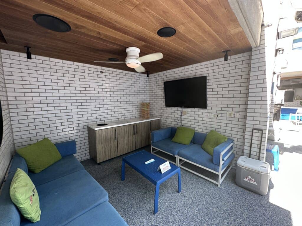 Inside look of cabana.  Showing mounted flat screen tv, blue couches coffee table.  Storage cabinet back of cabana