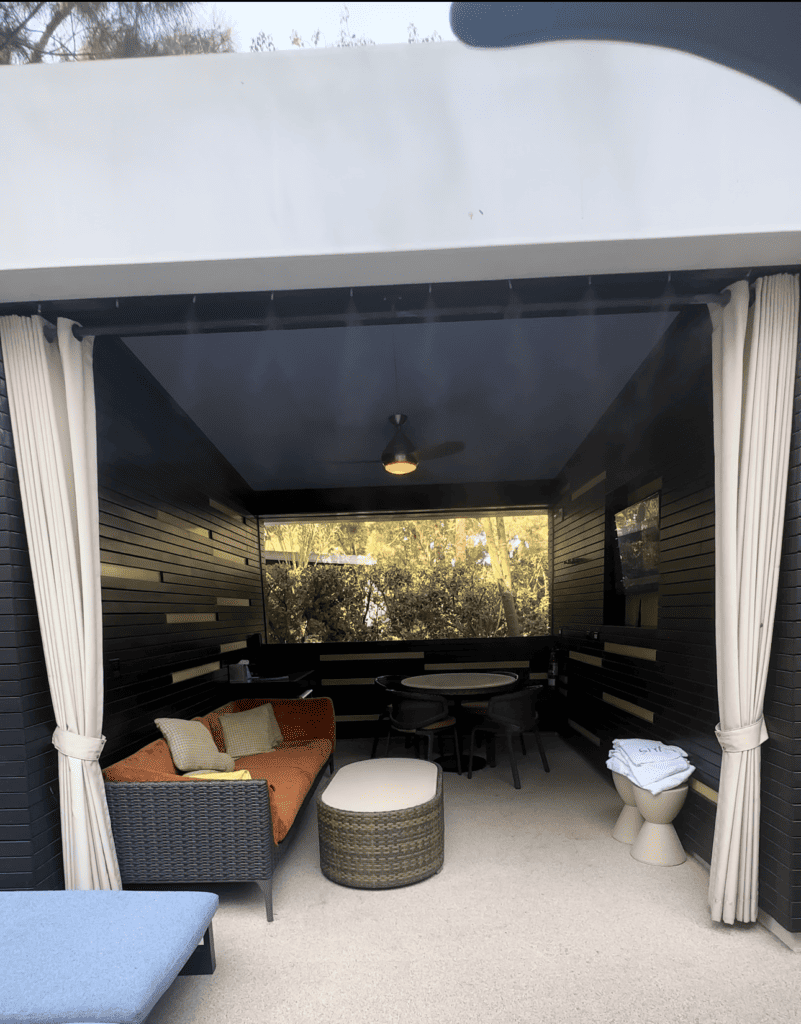 Looking into a cabana you can see a mounted TV with seating , a table and storage