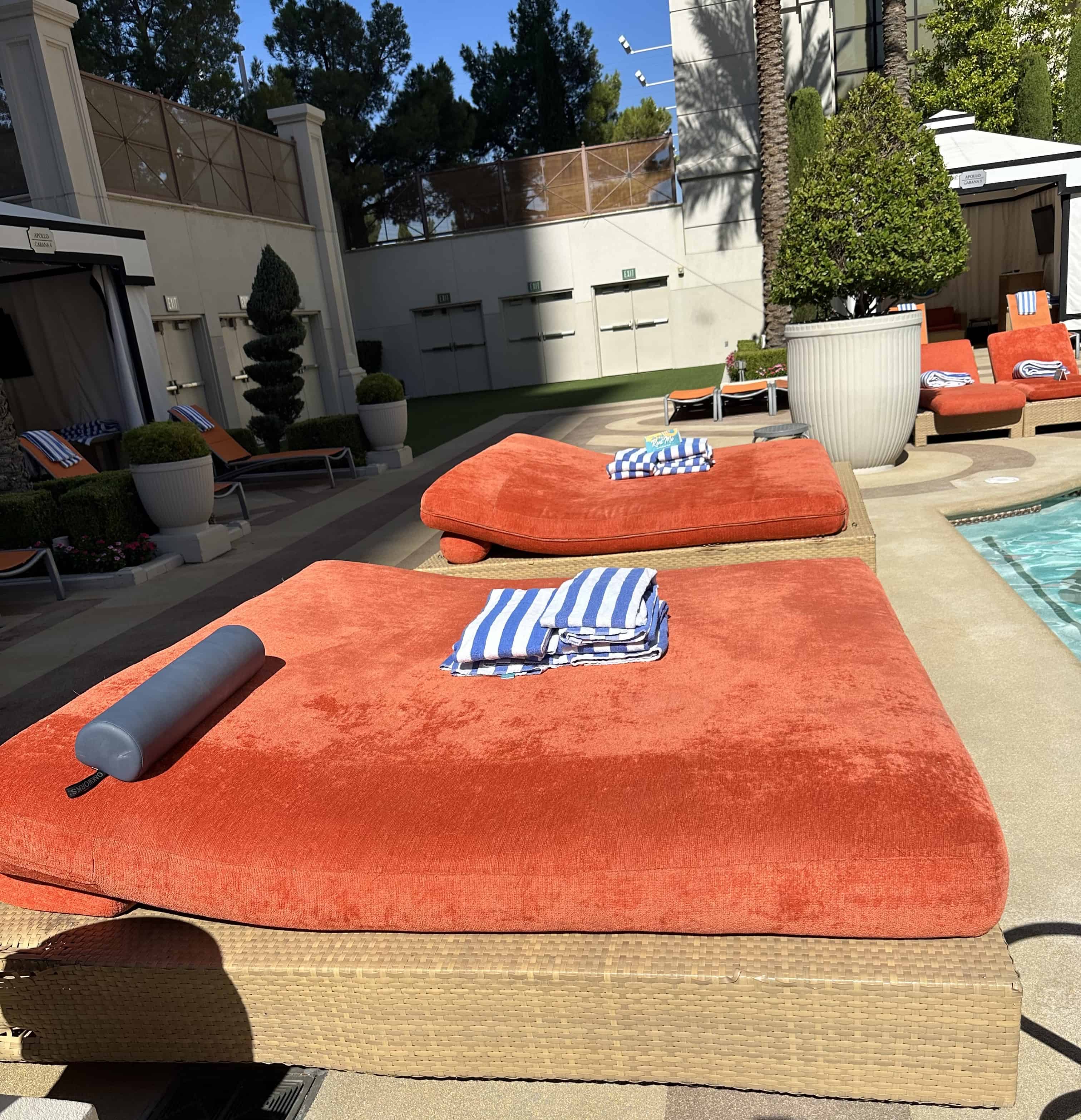 Two bright red daybeds alongside a pool. Striped towels are on both daybeds.