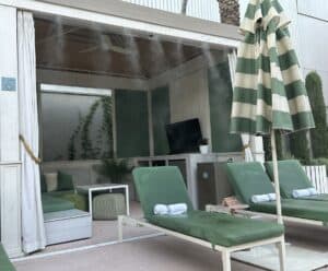 Looking into a cabana you can see two green loungers on the outside  and the misting system in operation.