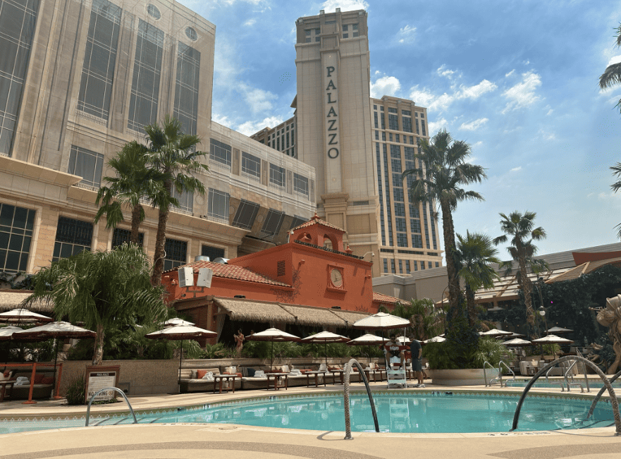 Tao Beach Club pool in the foreground and daybeds with sun umbrellas along the pool's side. The Palazzo tower is seen in the Background