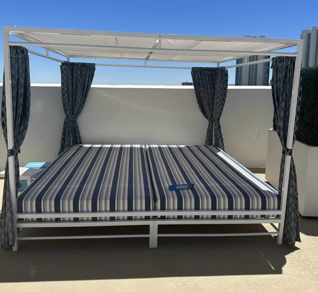 The Strat pool canopy daybed. White and blue striped queen size mattress with white cloth overhead cover.