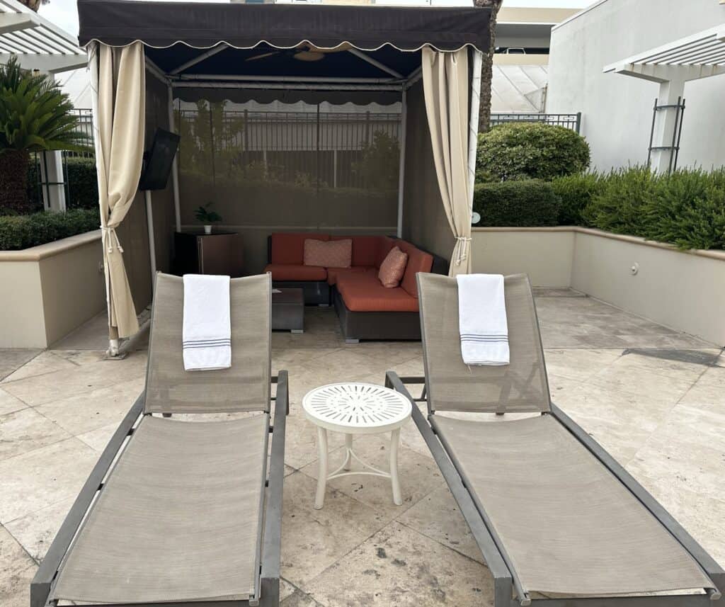 Looking into a cabana, there are two loungers outside with orange seating and storage on the inside.
