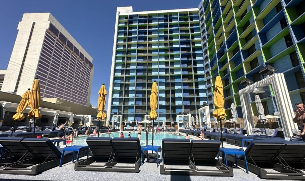 Daybeds are set up in front of the pool. Closed yellow sun umbrellas are next to each daybed. 
