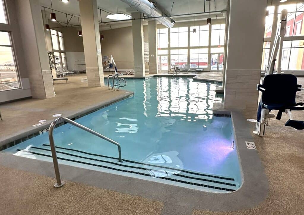 Indoor pool with large floor to ceiling windows along the back wall.