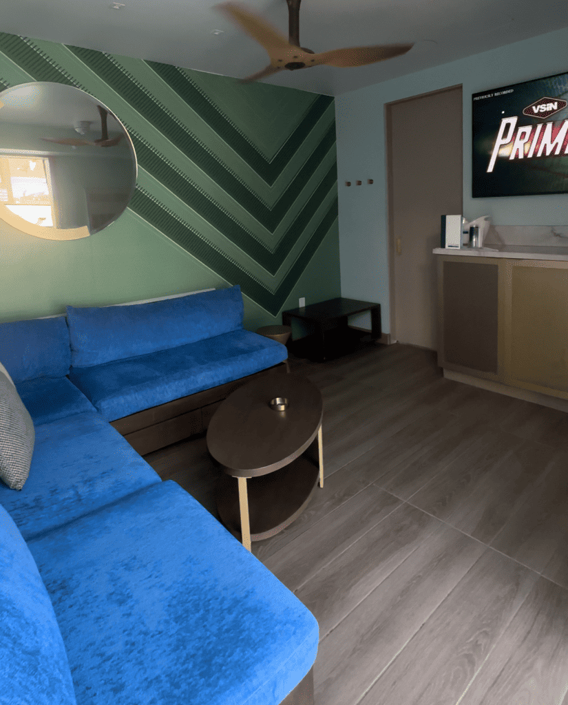 Inside cabana is a blue sectional couch along with storage and a mounted TV.