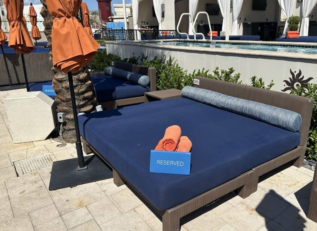 Blue cushioned daybed with rolled up red pool towels placed on it.