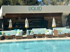 Light blue couch seating are with sun umbrellas between the pool and pool bar.