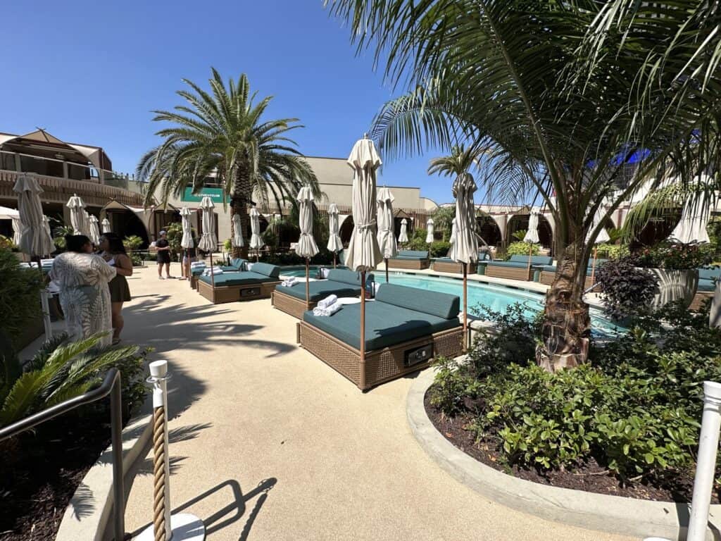 Daybeds are lines up by the pool. Palm trees are also around the pool.